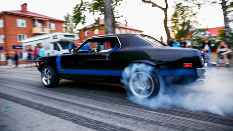 Black 70 Mustang with blue racing stripe doing a burnout